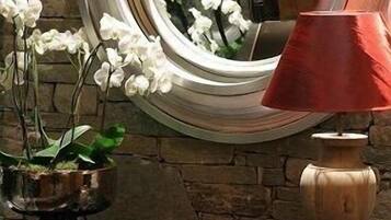 Un miroir rond avec un cadre en bois, une lampe rouge et des orchidées blanches sur un mur de pierre.
