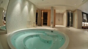 Una piscina interior moderna con una fuente de agua cristalina, rodeada por un diseño minimalista en tonos neutros e iluminación empotrada.