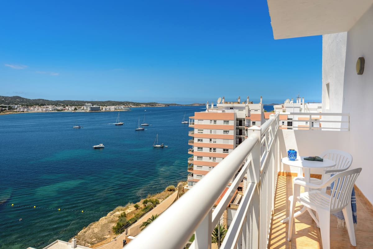 Uma varanda com vista para o mar, uma mesa com cadeiras e uma garrafa.