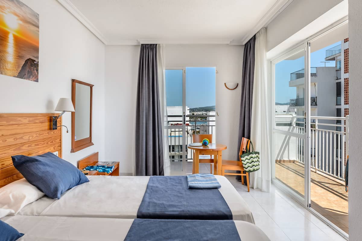 Quarto de hotel com duas camas, varanda, vista da cidade e área de refeições com mesa e cadeiras.