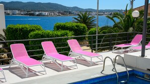 A poolside area with pink lounge chairs and a clear view of the sea and buildings in the background. - Aparthotel Vibra Sanan - Adults Only (Sant Antoni de Portmany)