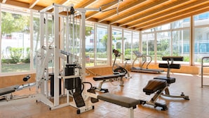 Un gimnasio con equipo de ejercicio diverso, ventanas amplias y techo de madera.