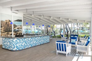 Amplio espacio interior con mostrador de recepción, mostrador de diseño azul y blanco, sillas blancas con cojines azules y vistas a una playa a través de amplias ventanas.