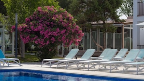 A poolside area with a clear blue pool, white lounge chairs, and a large bush with pink flowers. - Aparhotel Vibra Club Maritim (Sant Josep de sa Talaia)