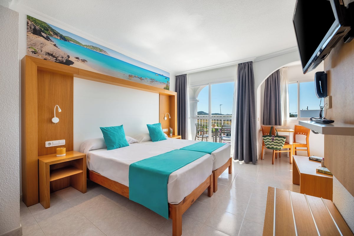 A hotel room with a large bed, a desk, a chair, a TV, and a window with curtains.