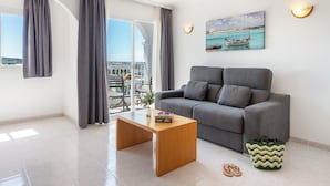 A modern living room with a grey sofa, a wooden coffee table, and a view of the sea through large windows. - Aparthotel Vibra San Marino (Sant Josep de sa Talaia)
