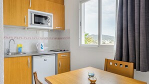 A compact kitchen with wooden cabinets, a microwave, a sink, and a small table with two glasses. - Aparthotel Vibra San Marino (Sant Josep de sa Talaia)