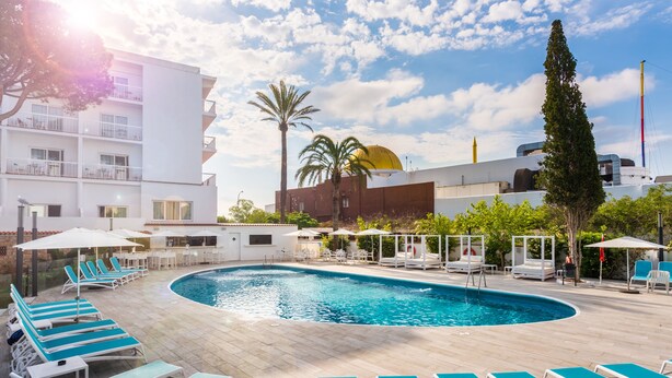 A swimming pool with sun loungers and umbrellas, surrounded by a building with balconies and palm trees. - Hotel Vibra Marco Polo I - Adults Only (Sant Antoni de Portmany)