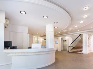Et hotellets reception med en buet disk, en trappe og et digitalt display.