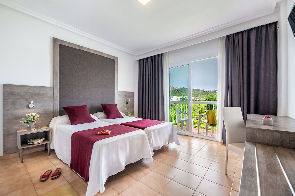Une chambre d’hôtel avec deux lits, un bureau, une chaise, une table de chevet et une vue sur l’extérieur.