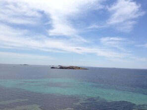 Vista costera con aguas turquesas cristalinas y una isla rocosa en la distancia.