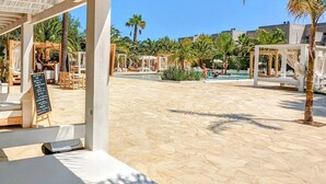 A covered outdoor area with a pool, lounge chairs, and palm trees. - The Palm Star Ibiza - Adults Only (Sant Josep de sa Talaia)