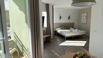 A hotel room with a bed, a bedside table with a fruit bowl, a chair, and a balcony with a chair.