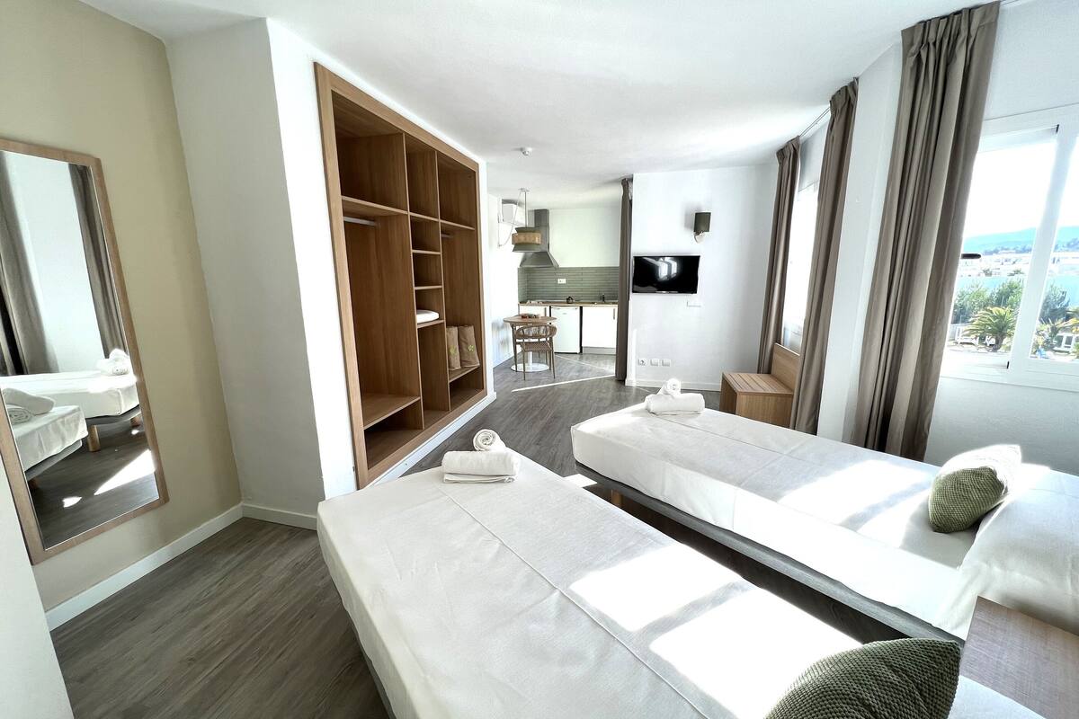 A hotel room with two beds, a wardrobe, a TV, and a view of the outside.