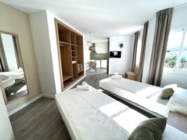 Quarto de hotel com duas camas, um guarda-roupa, uma televisão e vista para o exterior.