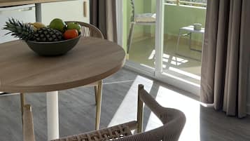 A modern kitchen with a dining area, a large window with a view of palm trees, and a balcony with a chair.