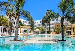 Piscina cercada por palmeiras e edifícios brancos com varandas.