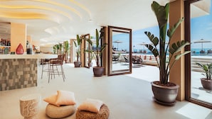 A modern hotel lobby with a bar area, seating, and large potted plants. - AMA Ibiza Suites - Adults Only (Sant Josep de sa Talaia)