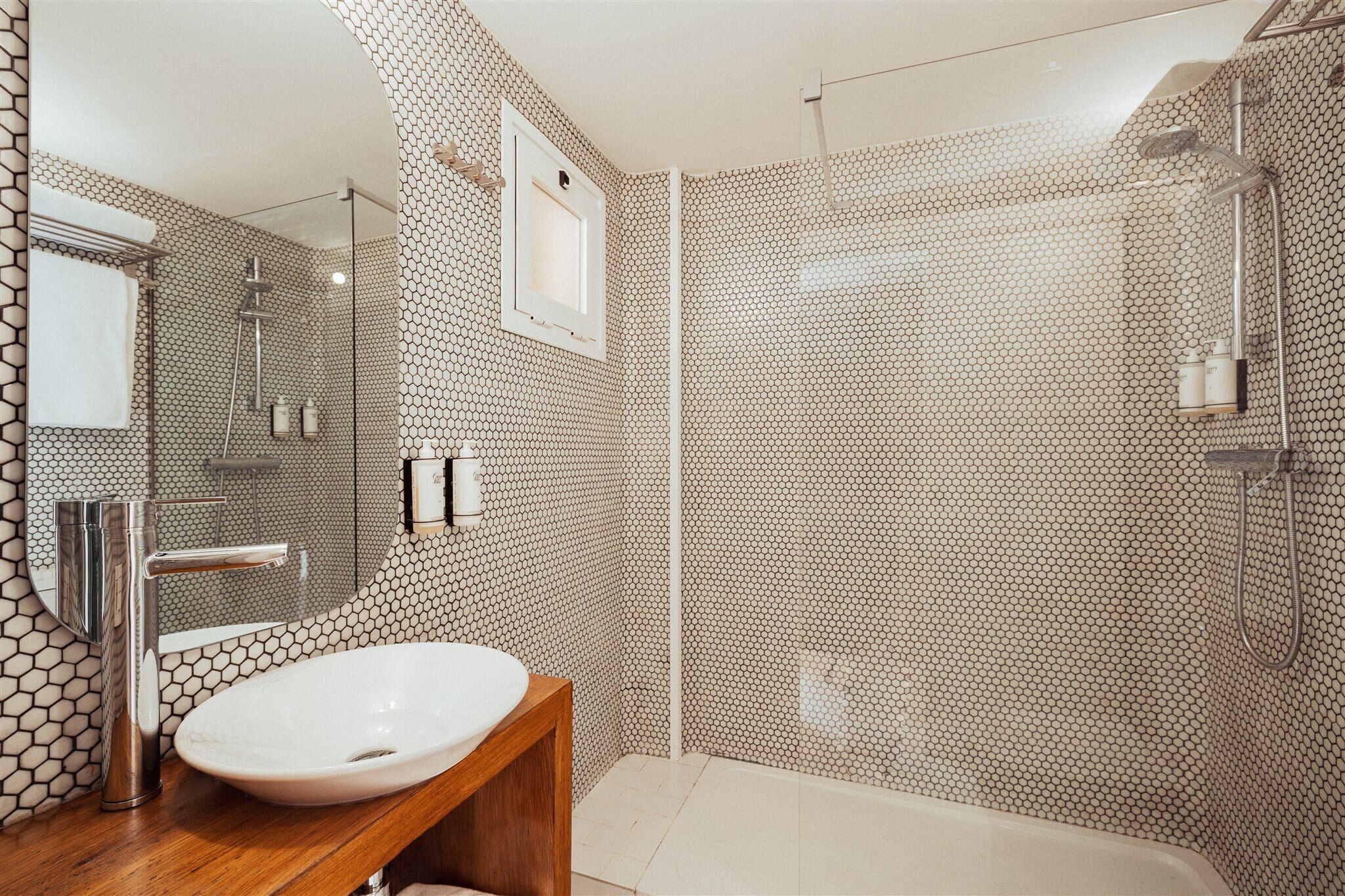 Un baño moderno con un diseño de baldosas hexagonales, un lavamanos redondo, un espejo y una cabina de ducha.
