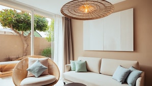 A modern living room with a sofa, a wicker chair, and a round table. - AMA Ibiza Suites - Adults Only (Sant Josep de sa Talaia)