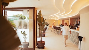 A hotel corridor with potted plants, a bar area, and a person walking. - AMA Ibiza Suites - Adults Only (Sant Josep de sa Talaia)
