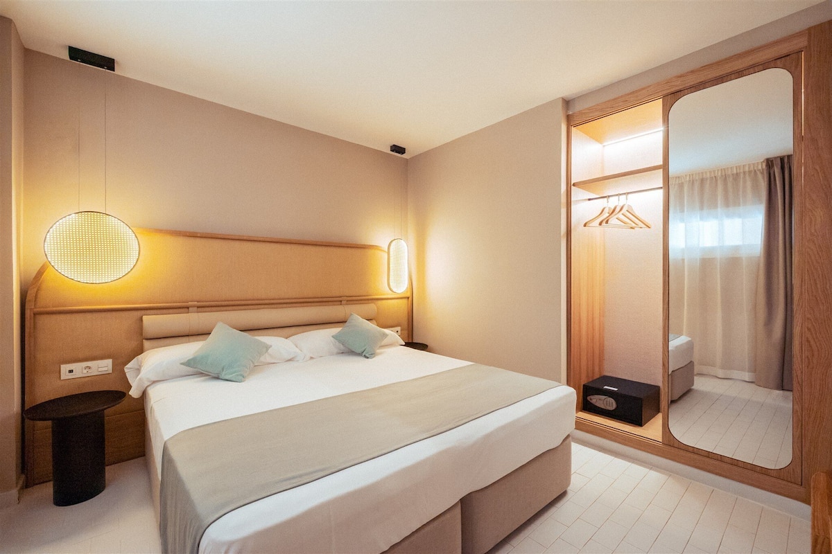 A hotel room with a bed, bedside table, and a large mirror.