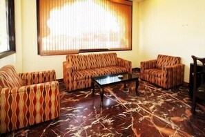 A living room with patterned sofas, a coffee table, and a large window with blinds.