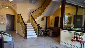 A grand staircase with ornate railings, a sitting area with patterned sofas, and a reception desk with a decorative figure. - Hotel Amer View (Amer)