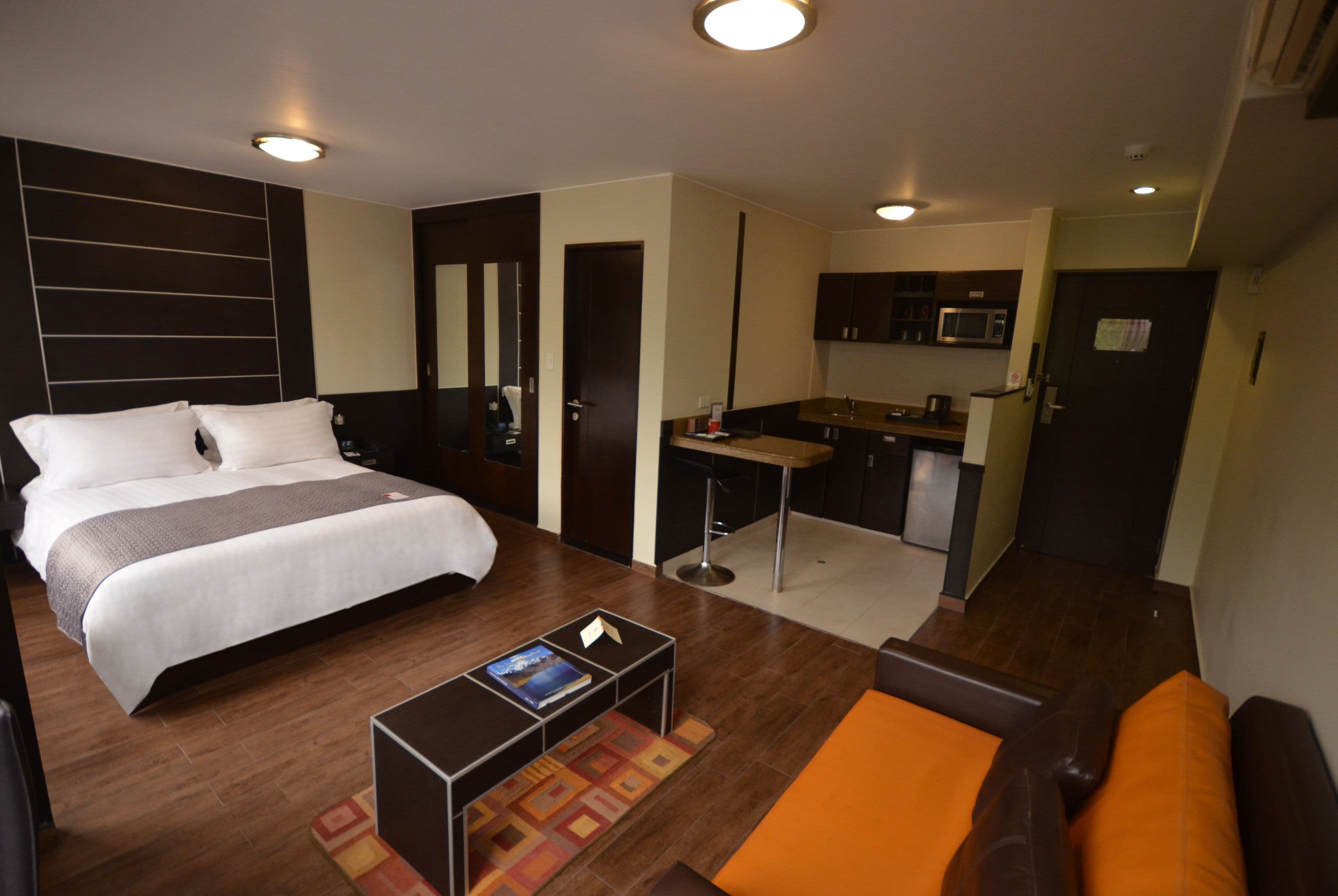 A hotel room with a bed, a desk, a kitchenette, and a seating area.