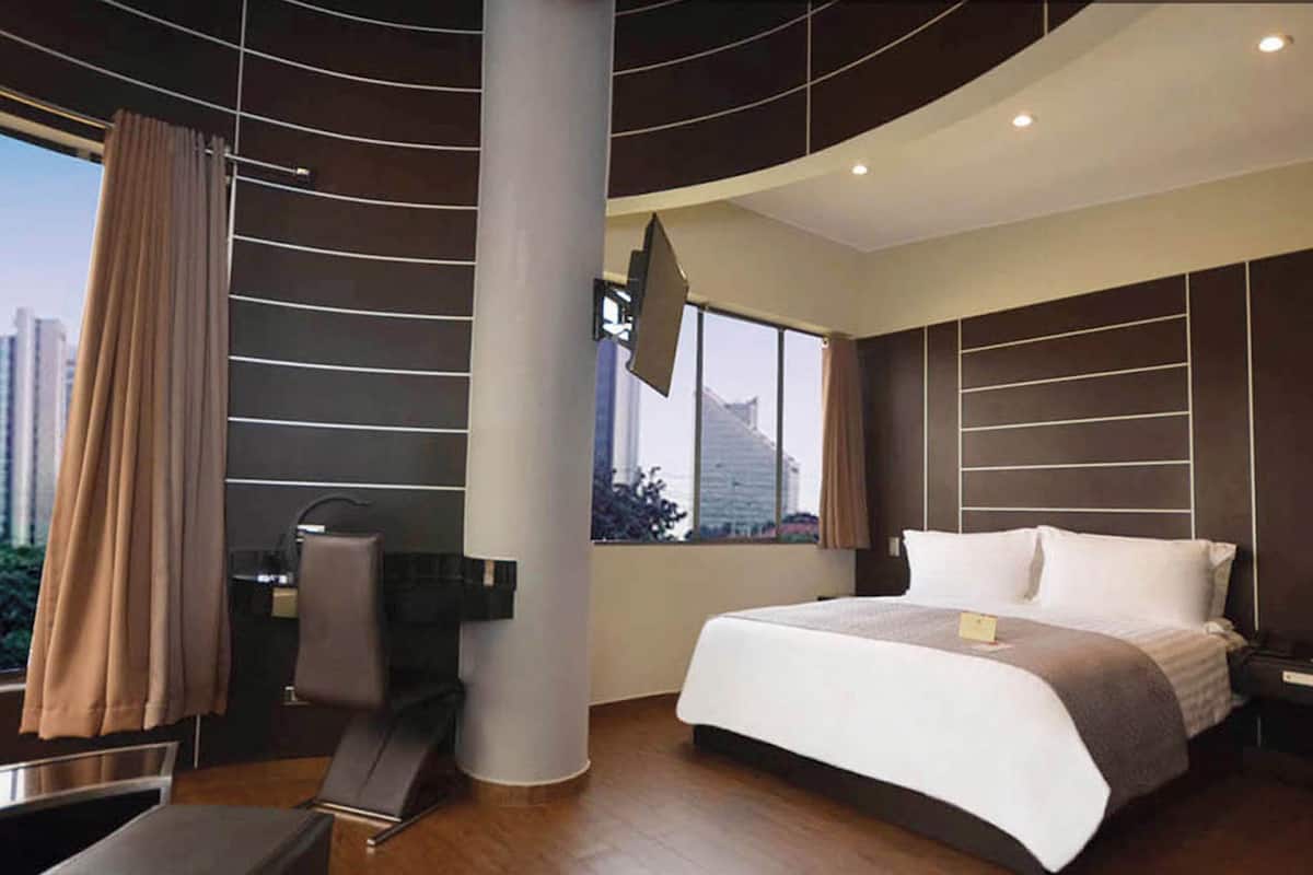 Ein modernes Hotelzimmer mit einem großen Bett, einem flachbildfernseher an der Wand, einem Schreibtisch mit Stuhl und einem großen Fenster mit Blick auf die Stadt.