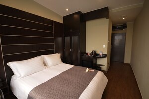Habitación de hotel con una cama grande, un escritorio con silla y una puerta que da a otra habitación.