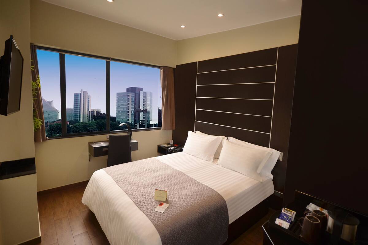 Ein modernes Hotelzimmer mit einem großen Bett, einem Schreibtisch und Blick auf die Stadtlandschaft.
