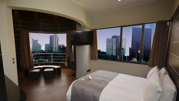 Habitación de hotel con una cama grande, televisión, balcón con vista a la ciudad y zona de estar.