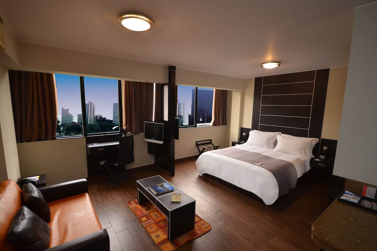 Ein modernes Hotelzimmer mit einem großen Bett, einem Schreibtisch, einem Fernseher und Blick auf die Stadt.