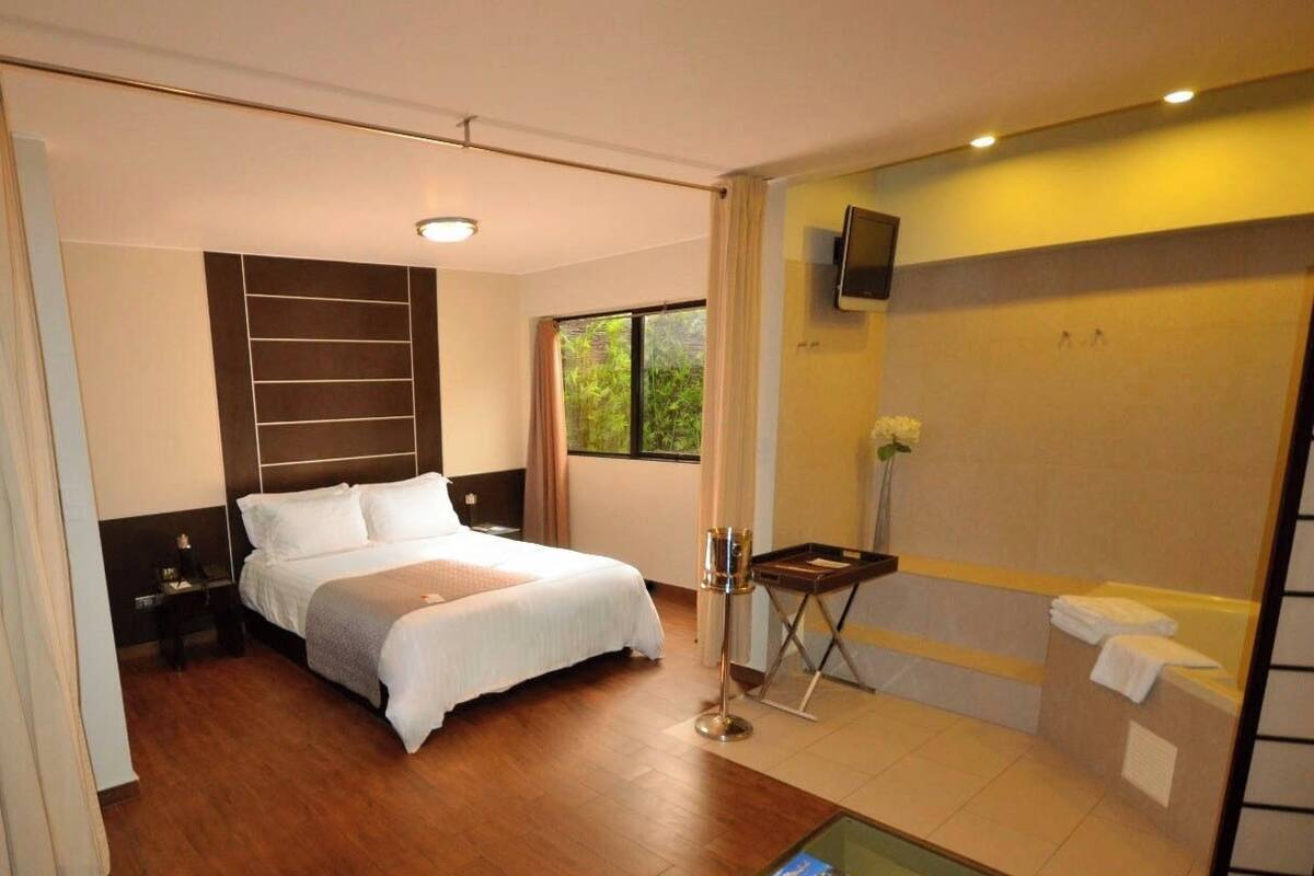 Ein Hotelzimmer mit einem Bett, einem kleinen Tisch mit einem Buch, einem Fernseher und einem Badezimmer mit einer Badewanne.