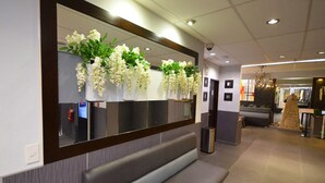 Zona de recepción con un banco, un espejo adosado a la pared y arreglos florales colgantes.