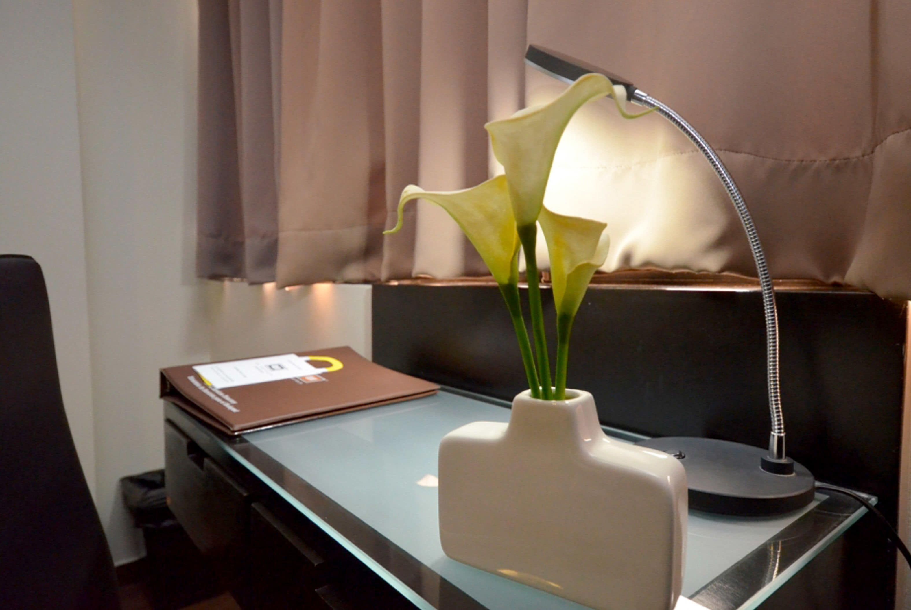 A desk with a vase of calla lilies, a laptop, and a desk lamp.