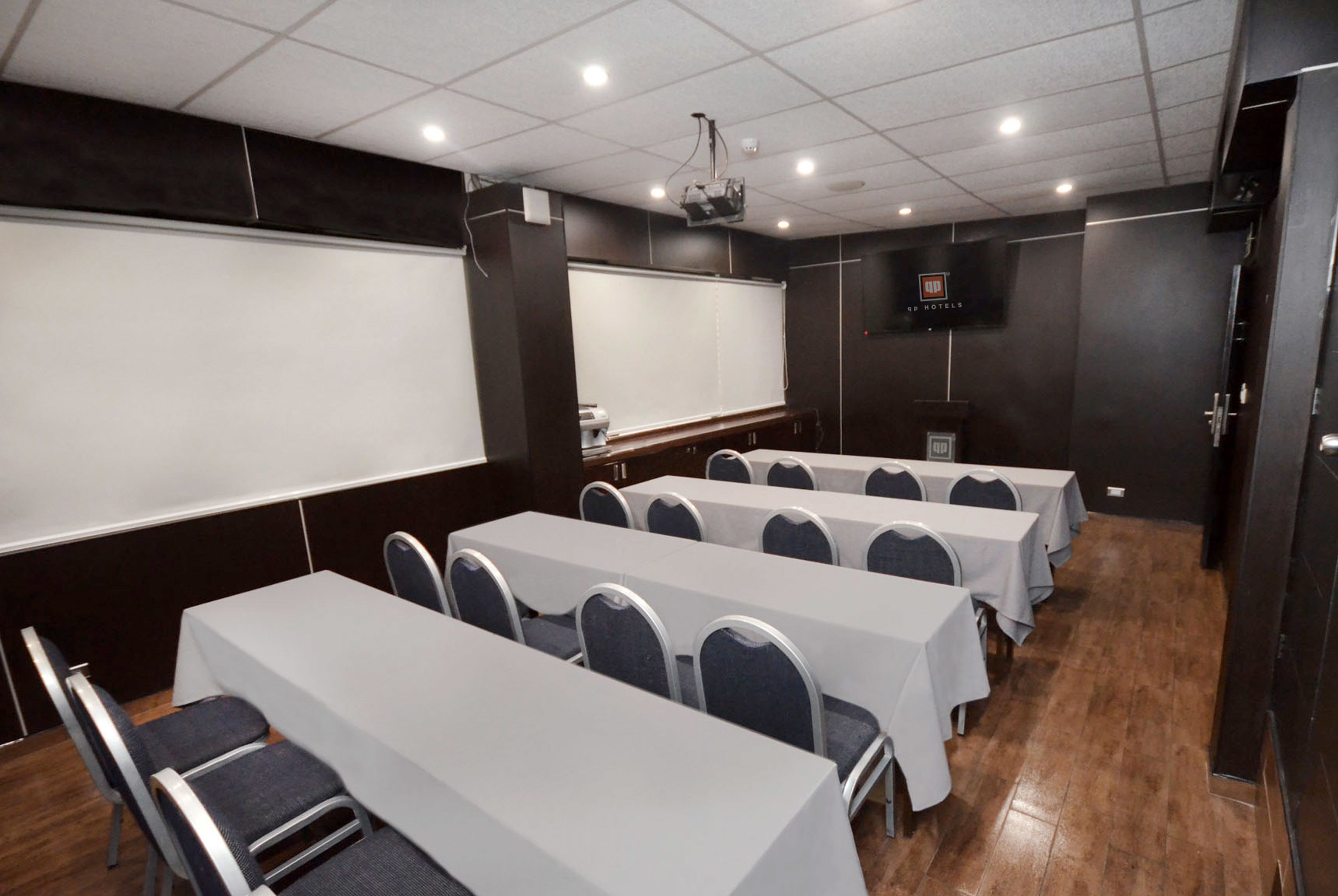 Ein Konferenzraum mit mehreren Tischen und Stühlen, einer Whiteboard-Tafel und einer Projektionsleinwand.