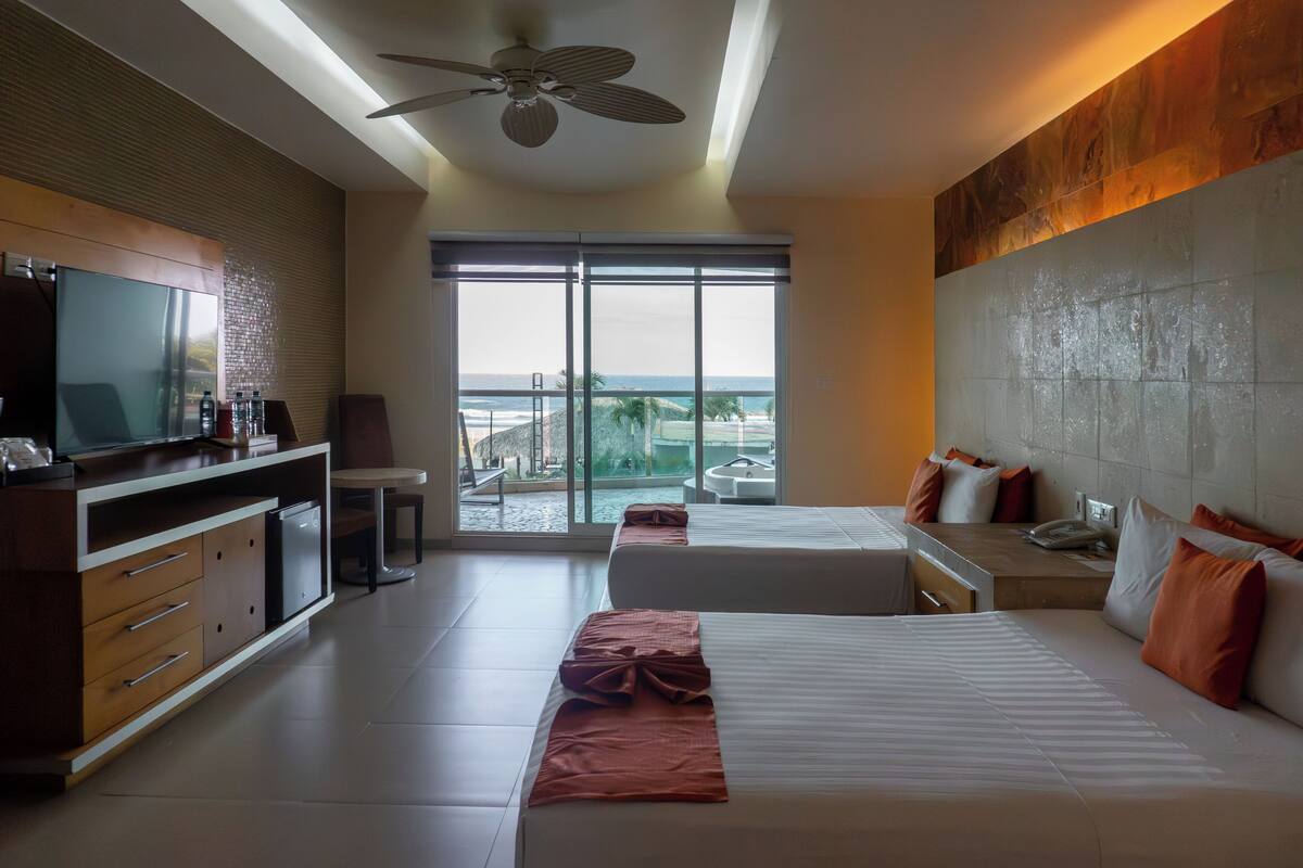 Habitación de hotel con una cama grande, un escritorio, un televisor y vista al océano.