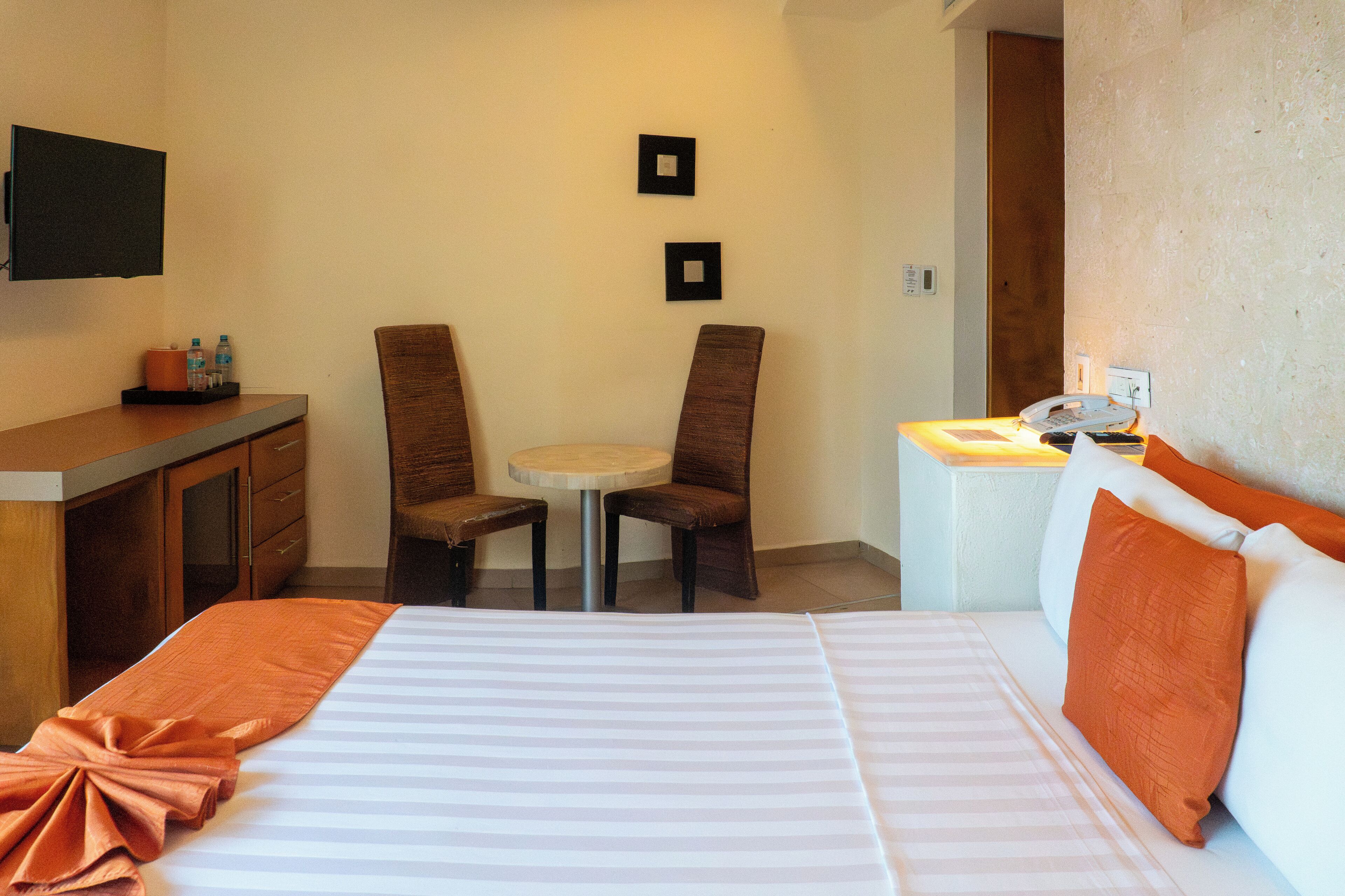 Une chambre d’hôtel avec un lit, deux chaises, une petite table et un téléviseur fixé au mur.