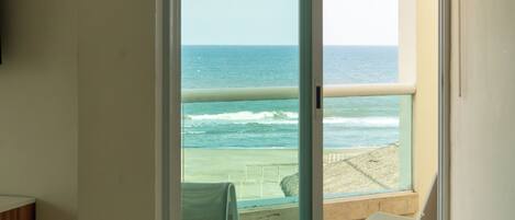 A room with a large sliding glass door leading to a beach view.