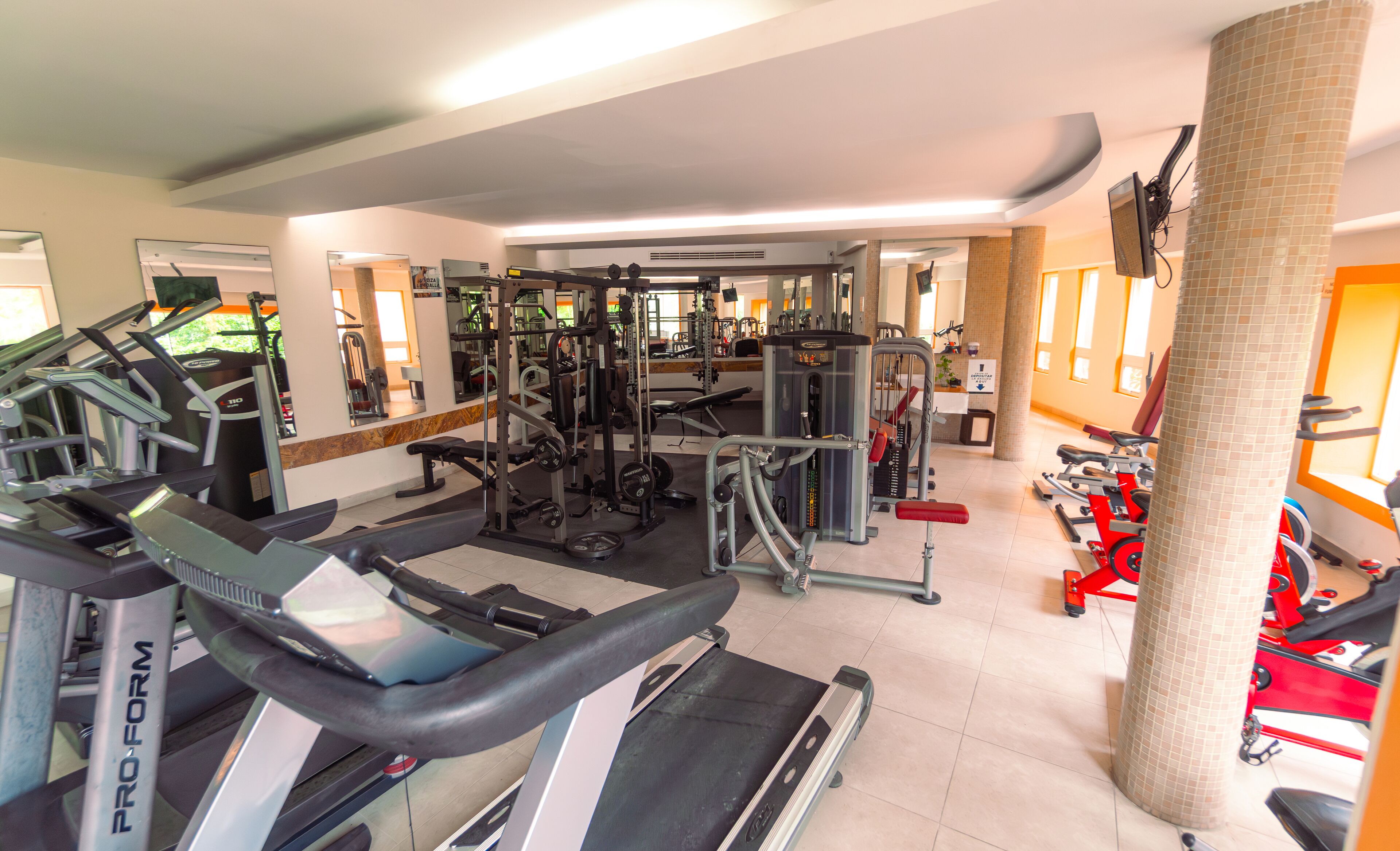 Ein Fitnessstudio mit Laufbändern, Kraftgeräten und einer Spiegelwand.