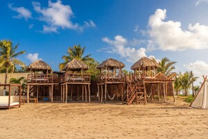Un resort en la playa con estructuras de techo de paja, pasarelas de madera y palmeras.