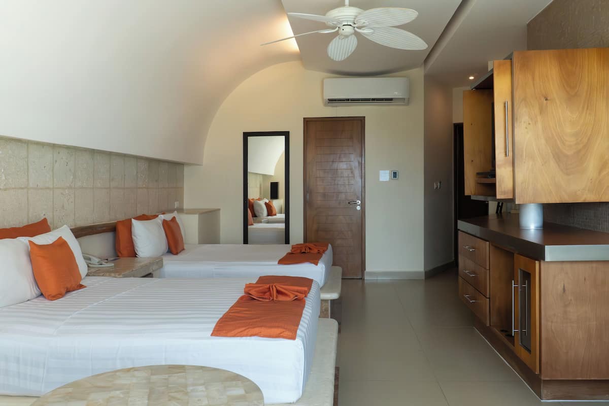 Habitación de hotel con dos camas, un armario de madera, un ventilador de techo y una puerta.