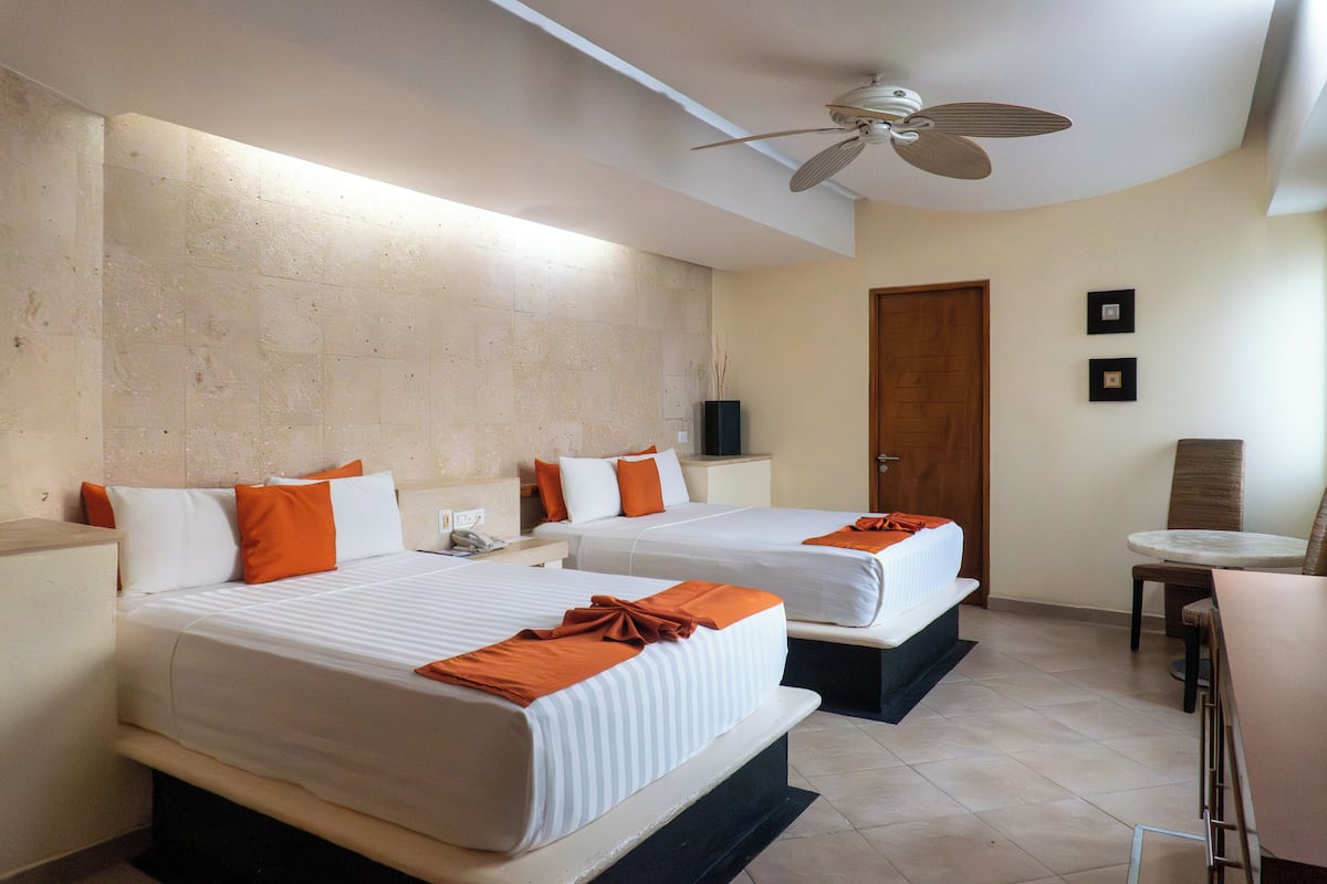 Habitación de hotel con dos camas, ventilador de techo, una mesita y una puerta.
