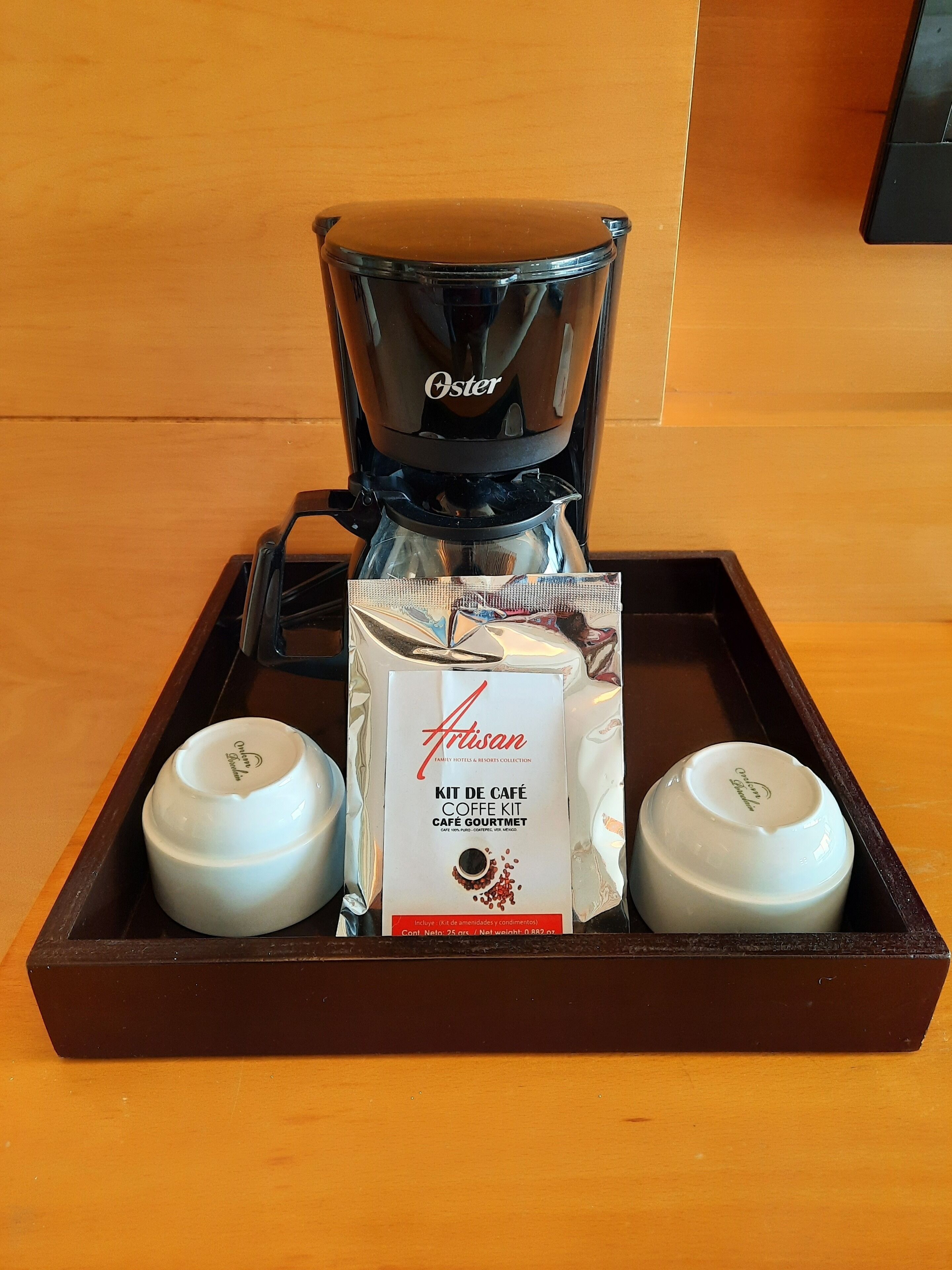 En kaffemaskine, en kaffekapsel og to kopper på et fad.