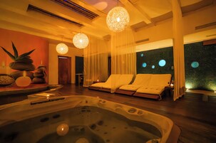 Un cuarto de spa con una bañera de hidromasaje, dos sillones blancos y un ventanal con diseños circulares.