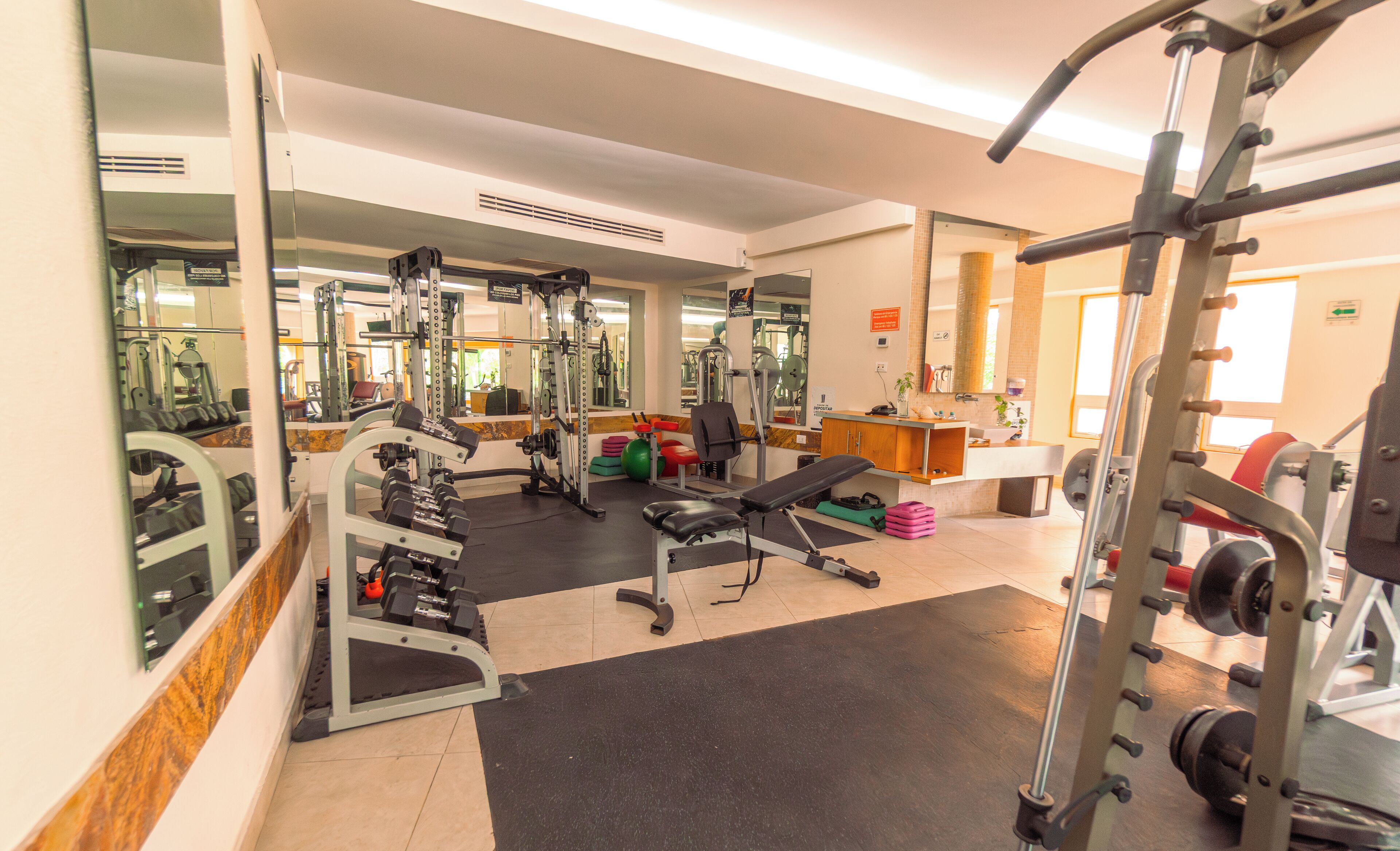 A gym with various exercise equipment, a bench, and a mirror.
