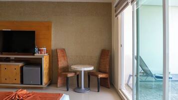 Une chambre d’hôtel comprenant un lit, une télévision, un petit réfrigérateur, une table avec deux chaises et un balcon avec un fauteuil.