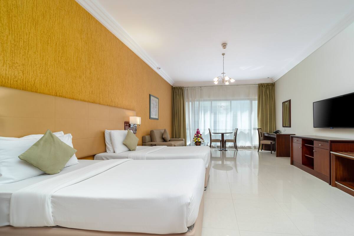 A hotel room with two beds, a TV, a desk, and a dining area.